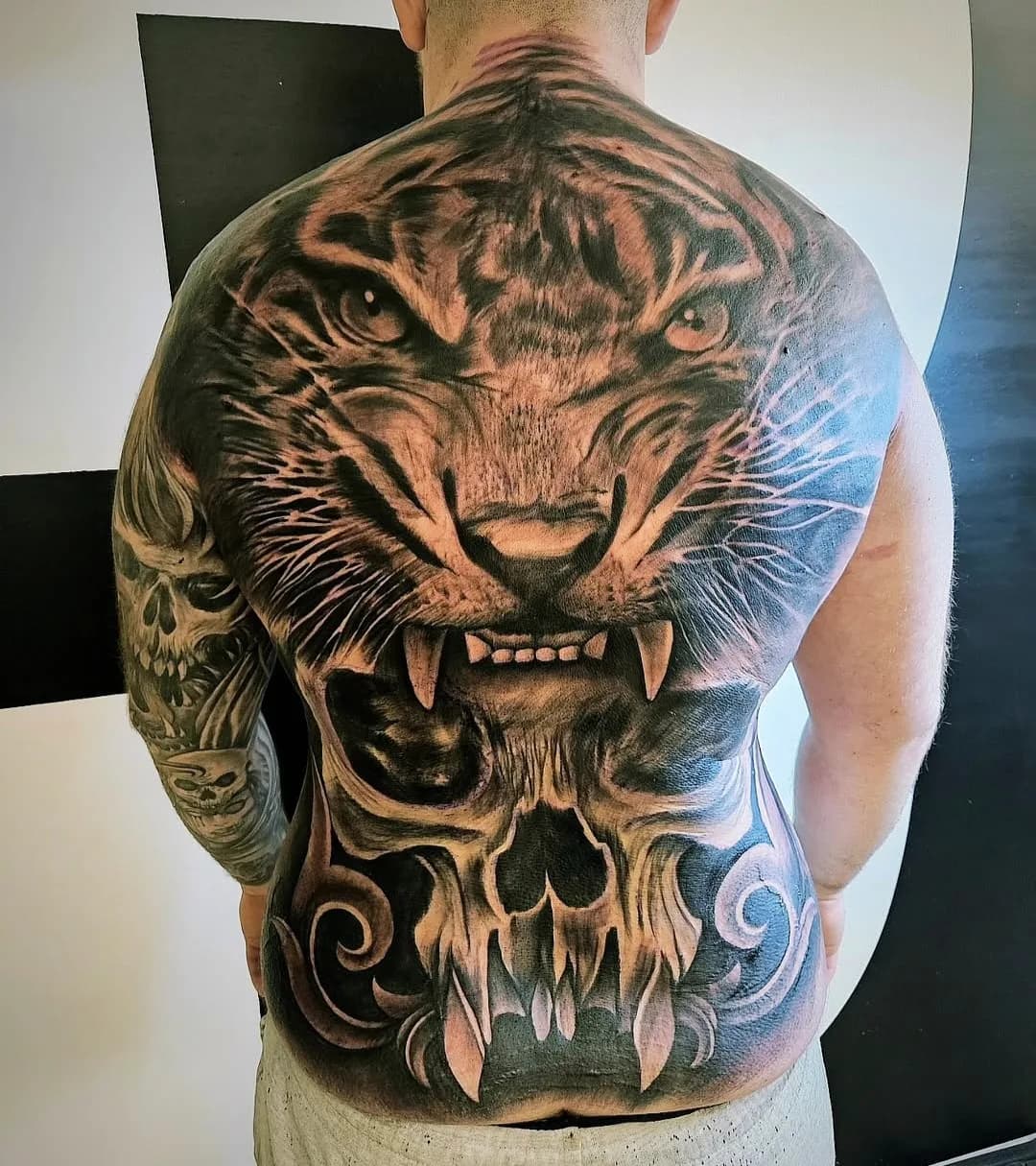 Ryggtatuering: tigerhuvud som övergår i en dödskalle med prydnadsslingor.